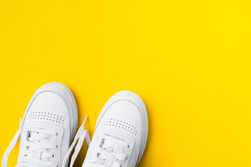 Pair of female stylish white casual sneakers on yellow background