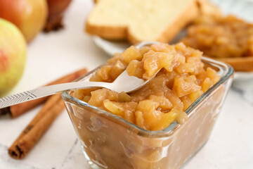 Bowl and spoon with sweet apple jam on light background