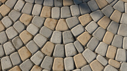 gray-beige natural processed stone in the structure of a paved pavement as a textured relief background, a top view of the surface of a city square with a semicircular laying of cubic blocks