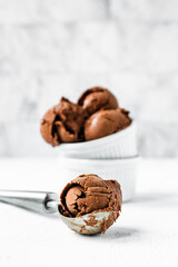 A chocolate ice cream ball in a scoop and ice cream in a white bowl, light and bright background