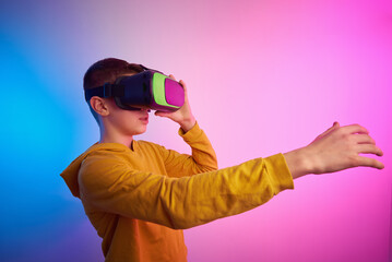 Boy with virtual reality glasses on colorful background. Future technology, VR concept