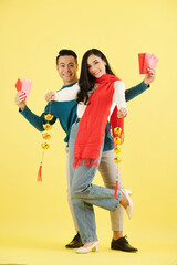 Happy beautiful young Asian couple in winter clothes showing lucky money envelops and garlands of sycee or Chinese gold ingots