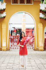 Obraz premium Attractive young Asian woman in traditional clothing walking with blooming peach branches in hands and smiling at camera