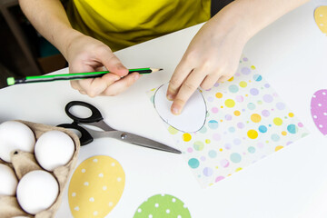 The concept of preparation for Easter. View from above on the white table with eggs, children's hands cut out of colored paper eggs.