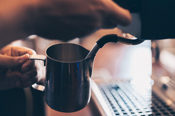 Barista heats milk steam for making lattes at coffee shop.