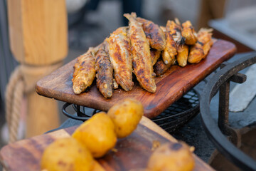 Crispy yellow potato and breaded european smelt fish on wooden cutting board at summer outdoor food market: close up. Barbecue, gastronomy, cookery, street food concept