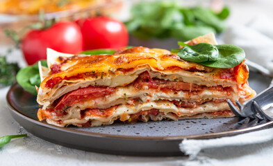 Italian lasagna with tomato sauce and cheese served with tomatoes and spinach, light concrete background. Homemade vegetarian lasagna.