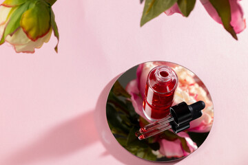 Glass bottle with oil on round mirror on pink background