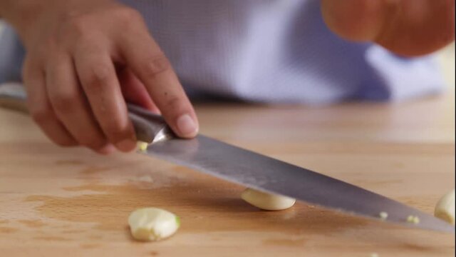 young wife chopping garlic in top of square chopping wooden board at kitchen table