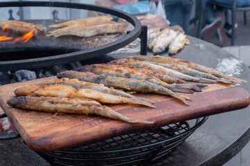 Crispy breaded european smelt fish on wooden cutting board at summer outdoor food market: close up. Seafood, barbecue, gastronomy, cookery, street food concept