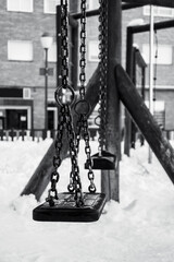 Swings in a snowy park on a cold winter morning. Black and white. Vertical view.