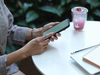 Female hands using smartphone on coffee table with beverage and notebook in cafe