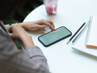 Female hands touching on smartphone on coffee table with beverage and notebook in cafe