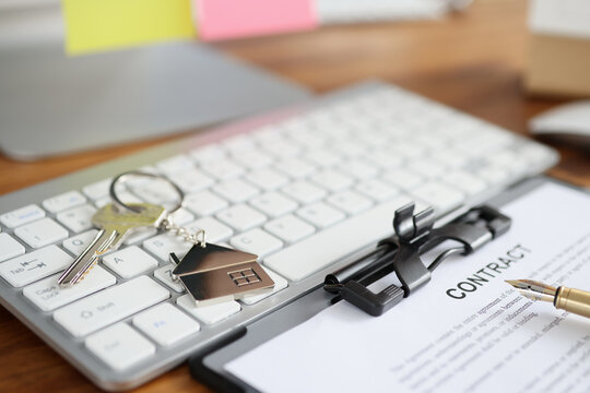 House keys and document with contract lying on keyboard closeup