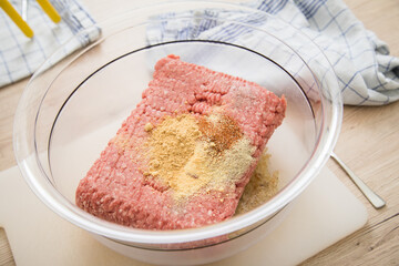 Hackfleisch halb und halb roh von Rind und Schwein mit gemahlenen Gewürzen in Schüssel auf Schneidebrett zum Kochen in Küche