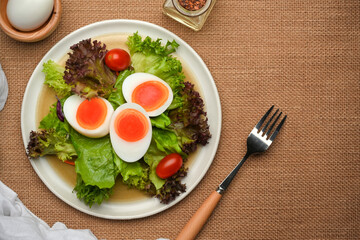 Plate of salad with boiled eggs, lettuce and tomato on placemat with fork