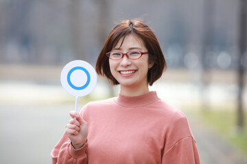 眼鏡を掛け〇札を持つ女性