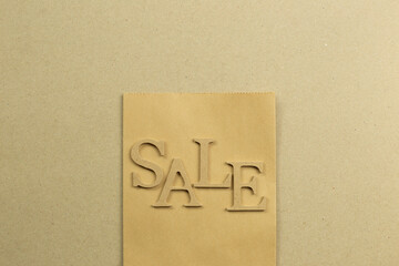 Shopping bag and 'Sale' word on brown kraft paper background. top view, copy space