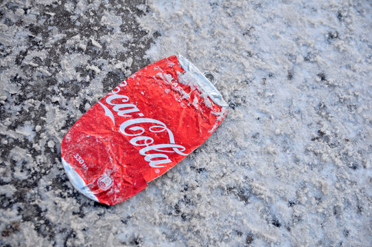 Coca-Cola can flattened under the wheels of cars on a winter road.