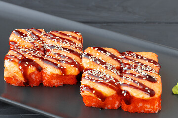 Baked sushi roll served on black plate on wooden table