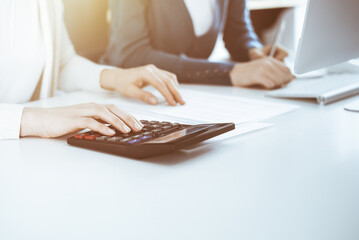 Accountant checking financial statement or counting by calculator income for tax form, hands close-up. Business woman sitting and working with colleague at the desk in office. Audit concept