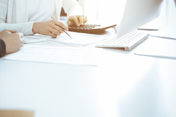 Accountant checking financial statement or counting by calculator income for tax form, hands close-up. Business woman sitting and working with colleague at the desk in office. Audit concept