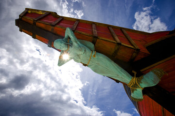 A Statue of a Mermaid Tied Up to the Bow of a Ship with Blue Sky and Clouds in the Background - obrazy, fototapety, plakaty