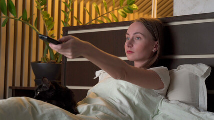Woman is lying on a bed watching a TV series late at night