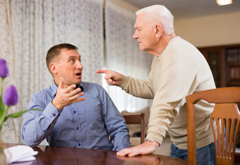 Annoyed elderly man and his adult son having conflict at home