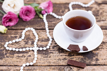 Morning time, beautiful picture for blog post in Instagram. Relax and have cup of coffee or tea with dark chocolate, decorate by flowers and beads as heart, enjoy your free minutes. Wooden background