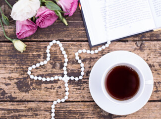 Morning time, beautiful picture for blog post in Instagram. Relax and have cup of coffee or tea with dark chocolate, decorate by flowers and beads as heart, enjoy your free minutes. Wooden background