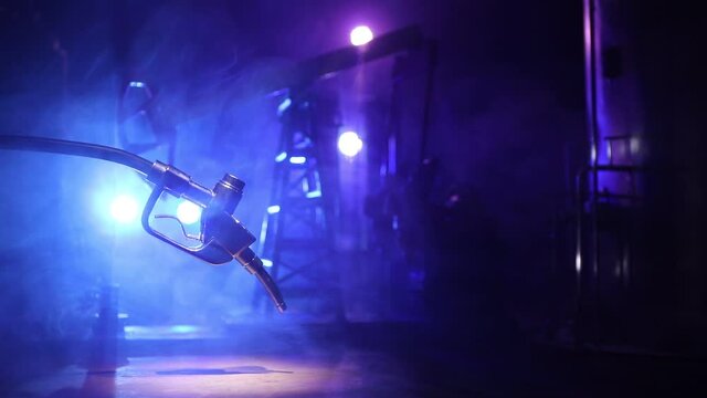 Creative concept. Silhouette of gasoline pistol miniature on dark toned foggy background. Close up. Oil pump and oil refining factory at night with fog and backlight on background. Selective focus