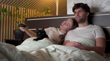 Couple watching TV at night at home lying on the bed