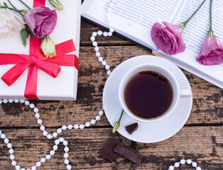 Morning time, beautiful picture for blog post in Instagram. Relax with cup of coffee with book and chocolate, decorated by flowers and beads, white gift box, enjoy your free minutes. Wooden background