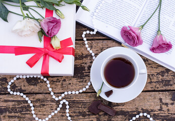 Fototapeta na wymiar Morning time, beautiful picture for blog post in Instagram. relax with cup of coffee with book and chocolate, decorate by flowers and beads, white gift box, enjoy your free minutes. Wooden background