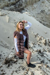 portrait of astonishing young woman wearing fur coat in dry empty sand quarry