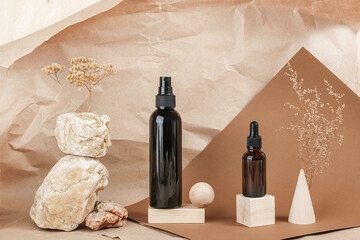 Brown glass bottles of cosmetic products on stone, wooden geometric shapes and dry flowers on beige paper background. Natural Organic Spa Cosmetic Beauty concept Front view Mockup
