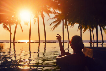 Vacation Beach Summer Holiday Concept. Silhouette woman relaxing in swimming pool on summer beach resort watching sunset.