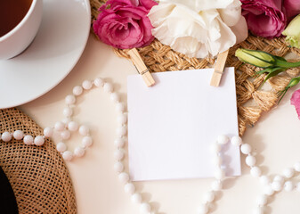 Unusual, beautiful composition for blog post in Instagram. Card for text on clothespins in center, flowers on brown napkin, cup of tea, beads and hat on white table. Free minute from rest. Closeup