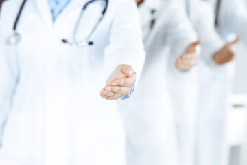 Group of modern doctors standing as a team whole offering helping hand for shaking hand or saving life. Medical help, insurance in health care, best desease treatment and medicine concept