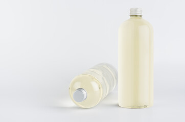 Set of two transparent plastic tall bottles standing and lying with pale fresh drink or cosmetic essential oil and silver cap, mockup on white background,  front and side view.