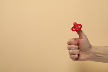 Female arm with red condom on beige background, space for text