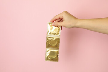 Female hand hold condoms on pink background, space for text