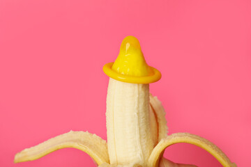Banana with condom on pink background, close up