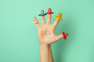 Female hand with text Sex and condoms on fingers on mint background