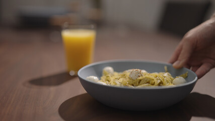 man put pesto fettuccine with mozzarella in blue bowl on walnut table