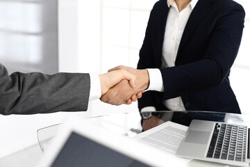 Unknown diverse business people are shaking hands finishing up meeting at the desk in office, close-up. Handshake concept
