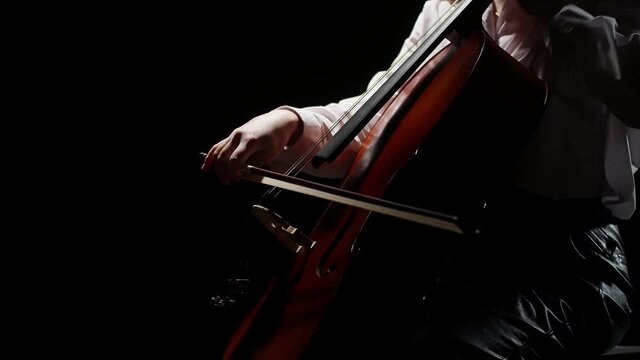 Musician plays with his hand using a bow on the strings of the cello in the darkness. Close-up artist plays on the violoncello.