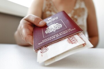 Woman is handing a Russian federation passport with Russian money, giving it to the camera sitting behind white table, close up and focus on the passport