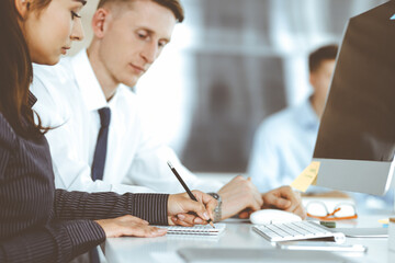 Business woman and man are discussing questions while using computer and blocknote in modern office, close-up. Teamwork in business